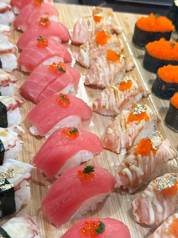 Stock photo showing close-up view of rows of nigiri sushi on wooden board in a sushi restaurant.