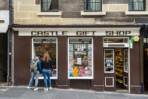 Royal Mile, Edinburgh, Scotland, August 2023. This is the Royal Mile early morning during the Edinburgh Fringe Festival.  There are tourists on the street looking into the Castle Gift Shop window.