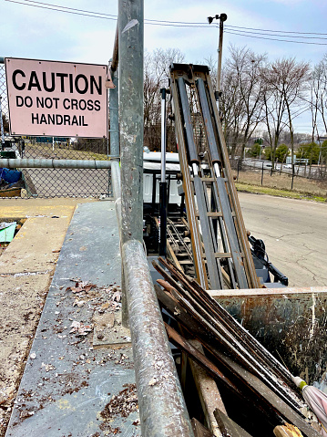 Fairfax, Virginia, USA - February 24, 2024: A “Caution Do Not Cross Handrail” warning sign next to an industrial sized container being lifted onto the back of a truck at Fairfax County’s “I-66 Transfer Station”.