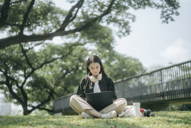 Asian students in black uniforms feel happy while sitting outdoors on the grass in the city