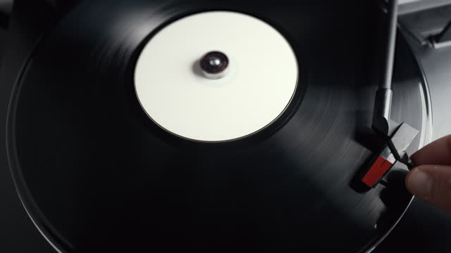 Hand holding the tonearm of the player and bringing it to starting track of the vinyl record