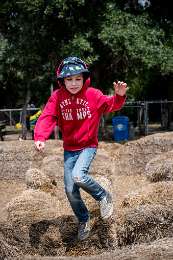In a scene straight out of childhood dreams, a boy delights in the simple pleasure of jumping across hay bales, embodying the carefree spirit of rural living