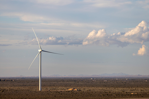 Two windmills in a wind energy farm in New Mexico. A towering white wind turbine stands tall over the rugged plains of West Texas and New Mexico.