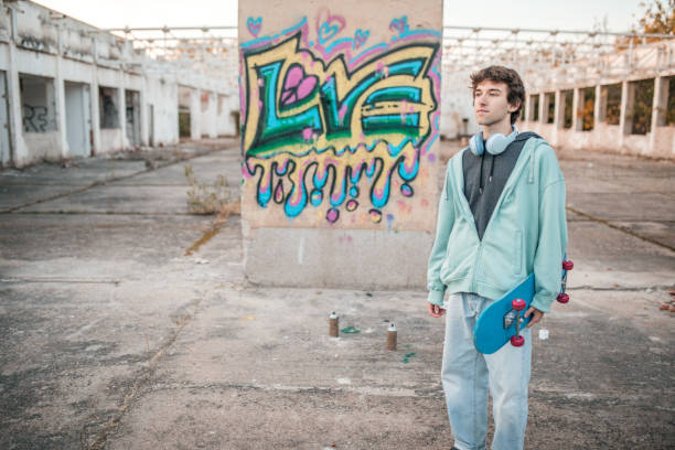 ein junger street-art-künstler steht neben einer wand, auf die er graffiti gemalt hat - graffiti men wall street art stock-fotos und bilder