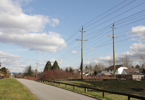 Utility poles line an easement in the Green Timbers Greenway in the Fleetwood-Tynehead neighbourhood of Surrey, British Columbia. Winter afternoon with clouds above Metro Vancouver.