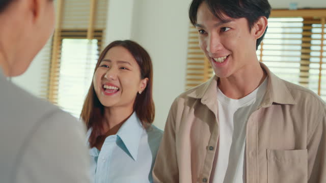Close-up of Asian female real estate agent explaining and showing living room in new house to tenants for rent or buy. Landlord selling real estate to happiness couple customer.