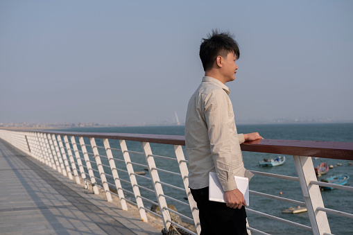 A man working outdoors holds the railing and looks at the sea