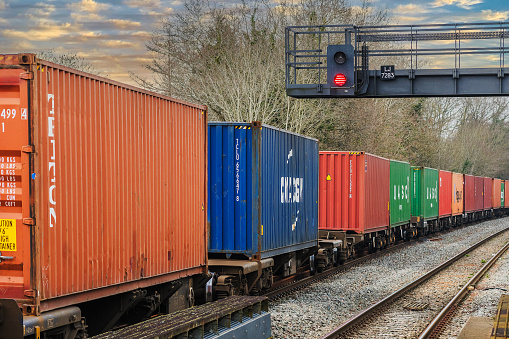 March 8th. 2024 A freight goods container train is passing through Dorridge Station West Midlands England UK. There are no visible people in the picture.