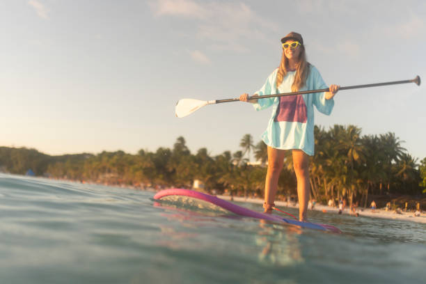 A cheerful woman enjoys stand-up paddle boarding, enjoys her vacation and the sea and peace and quiet