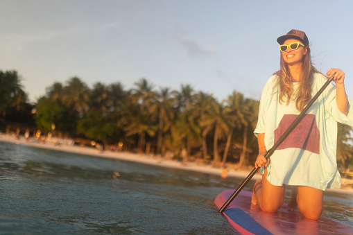 A smiling woman enjoys stand-up paddle boarding, enjoys her vacation and the sea and peace and quiet