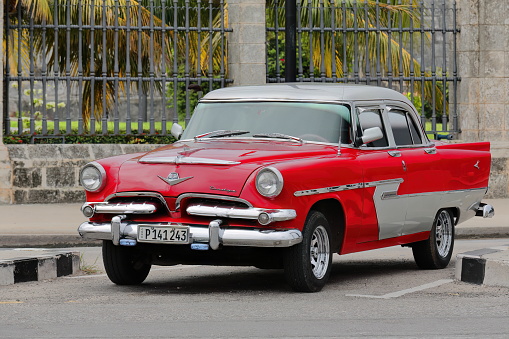 Havana, Cuba-October 7, 2019: Red-gray old American classic car -almendron, yank tank- Dodge Kingsway Custom 4 door Sedan of 1956 (1955 model's frontal grille) parks on Avenida del Puerto-Port Avenue.