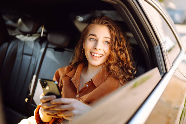 istock Young woman uses a smartphone while sitting in the back seat of a car. 2068871663