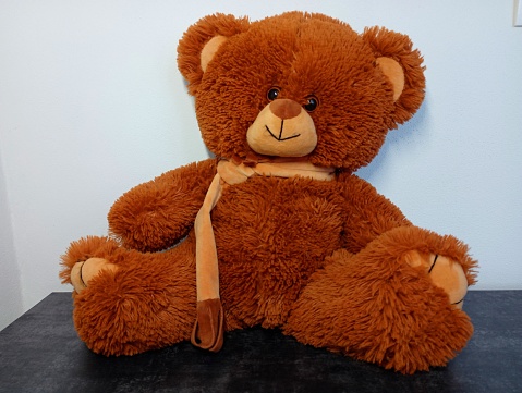 Children's soft toy brown bear on a white background sits on the surface of a gray bed. Themes of childhood and teddy bears.