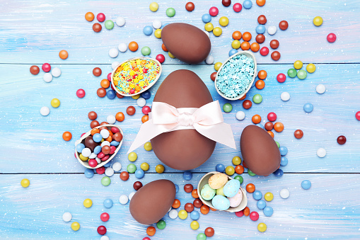 Easter chocolate eggs with candies and sprinkles on blue wooden table