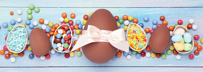 Easter chocolate eggs with candies and sprinkles on blue wooden table