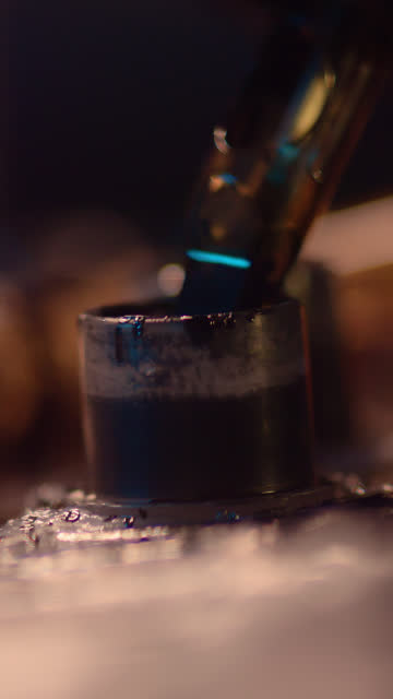 Extreme close-up of a tattoo machine. Needle going into a container to refill with ink.