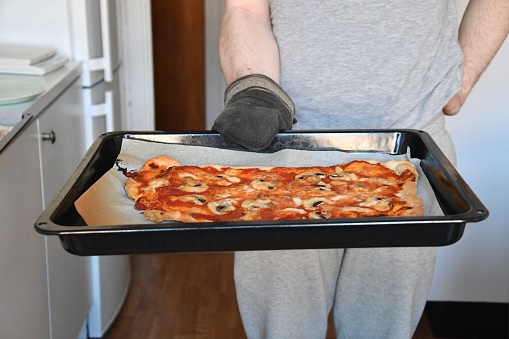 A man holding a hot plate with a homemade pizza on