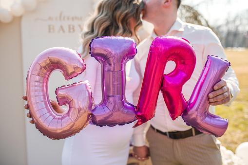 Future parents are standing in the park and holding balloons that say: It's a girl!