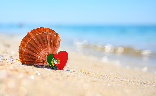 Sandy beach in Portugal. Portugal flag in the shape of a heart and a large shell. A wonderful seaside resort.