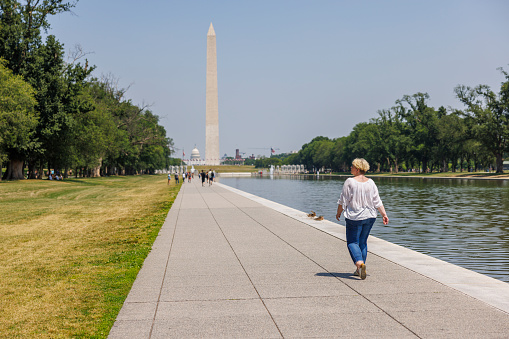 Solo tourism at Lincoln Memorial in Washington, D.C. Mature Caucasian blonde woman strolling on historical landmarks of America. The Capitol shown in the distance.