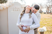 A loving couple stands in each other's arms in the park. They make a heart sign on the stomach of a pregnant woman