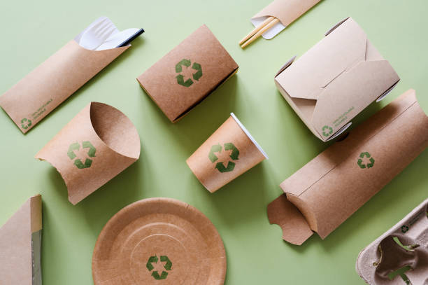istock Disposable tableware made from recycled cardboard on a green background. Food packaging with green recycling signs. 2069114114