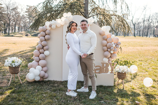 A loving couple stands in front of a baby shower decoration