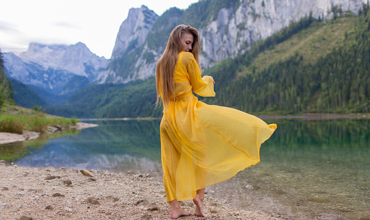 Beautiful girl in a light yellow dress by the lake in the mountains