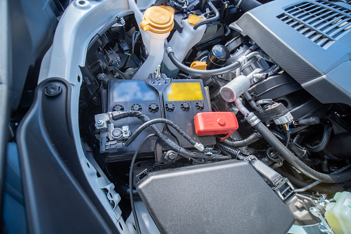View of car 12V battery under the hood in engine bay, electrical system, providing the power needed to start the engine.  Operation of various electrical components and service check up.