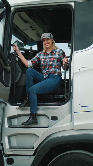 Vertical shot of a smiling woman trucker sitting in the cab and looking at the camera