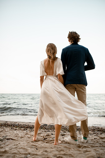 Young husband and his wife admire the sea, standing on the coast with their backs to the camera