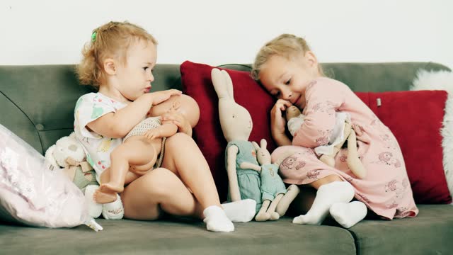 Little girls play with dolls on the sofa at home