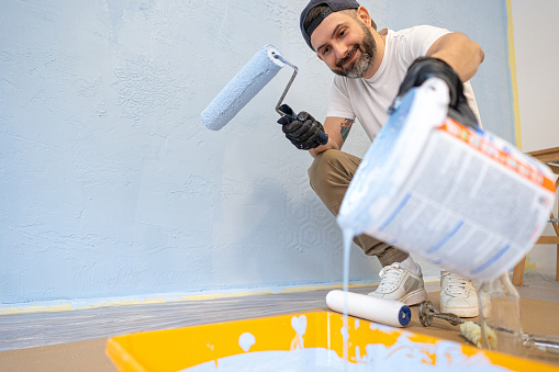Mid-adult Caucasian man, a handyman, preparing a light blue paint, while painting the apartment