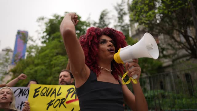 Transgender person leading protest and talking on megaphone outdoors