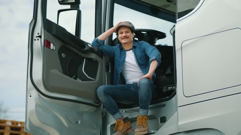 Portrait of happy truck driver man sitting in the cab and looking at the camera