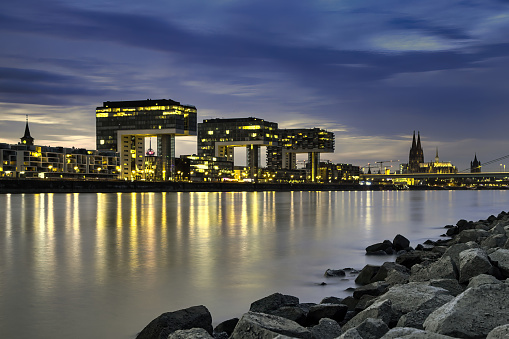 Cologne, Germany – September 28, 2023: Nighttime waterfront with illuminated waters and a large bridge spanning across, Colgne Rheinauhafen, Kranhaeuser with Cathedral and Serverinsbridge