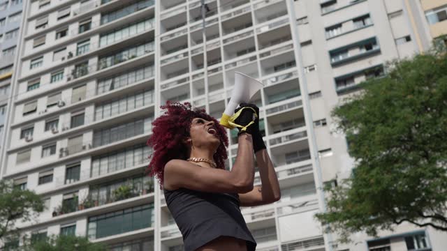 Transgender person talking in a megaphone at city street