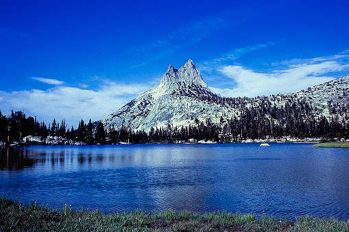 Cathedral Peaks under a cloudy sky with the lake in the foreground.\n\nTaken in Yosemite National Park, California, USA