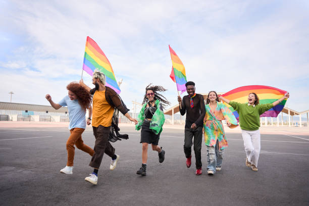 Group happy LGBT people walking down street with rainbow flags under clear sky
