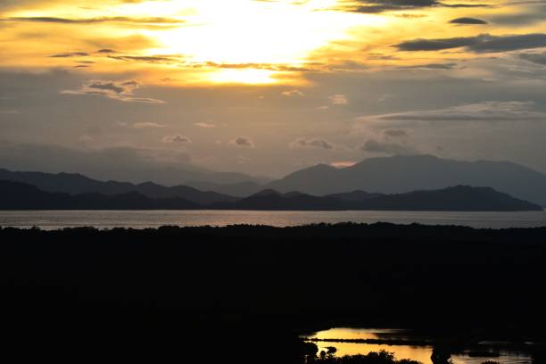 Clouds turn yellow as the sun sets behind mountains along the Tempisque River in Costa Rica.