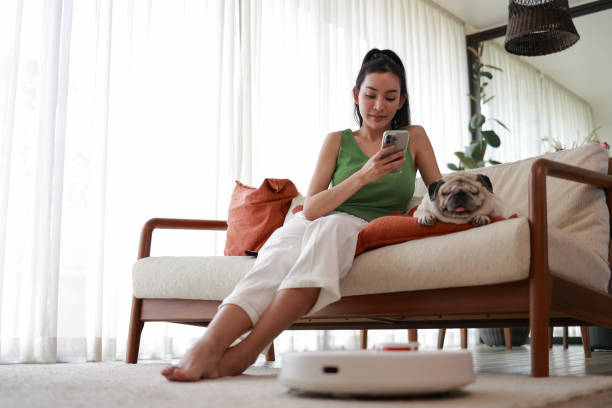 istock Woman Using Smartphone Next to Pug on Couch with Robotic Vacuum 2069440728