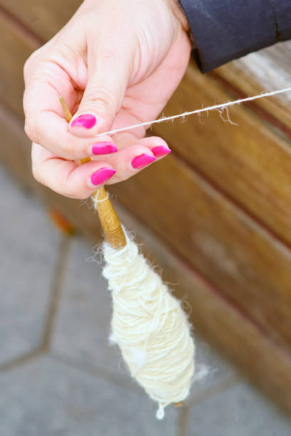 The woman is spinning yarn from wool using a drop spindle.