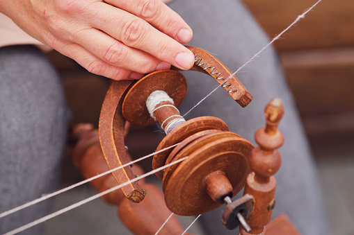 The closeup shot shows a hand spinning thread on a vintage spinning wheel. Close-up of a woman's hands weaving thread on a spinning wheel