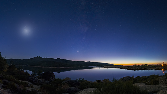 Colorful twilight with Crescent moon and planets Venus, Saturn, Jupiter and Milky Way over mountain lake, Vale do Rossim, Serra da Estrela, Portugal