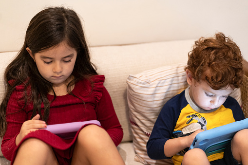 Two siblings igonring each other and watching each his own digital tablet