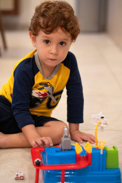 Little redheaded caucasian toddler three years old sitting on the floor playing with his new colorful car toy and looking straight at the camera