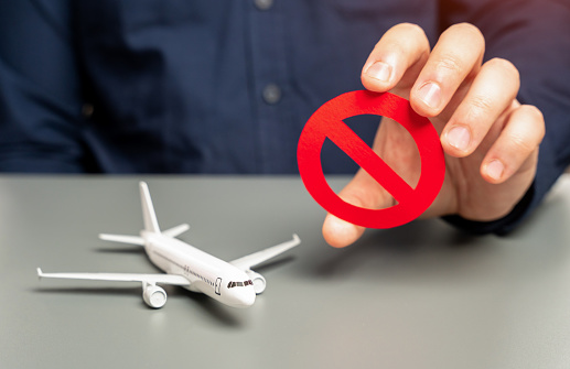 A man holds a prohibitory sign near an airplane. Sanctions. Refusal of aircraft insurance, breaking leasing agreements. Closing air routes. Flight cancellation. Failure safety tests. Restrictions