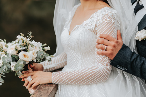 Wedding portrait. A brunette bride in a long dress and a groom in a classic suit are standing, embracing, in love against the background of a lake.