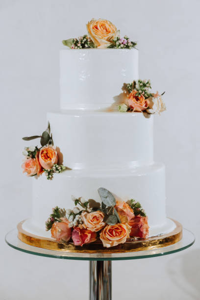 istock White three-tiered wedding cake decorated with orange roses. Festive dessert table with sweets. Wedding candy bar, various cakes, chocolate on stands. 2069629569