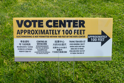 A multilingual voting center sign with arrow and instruction.